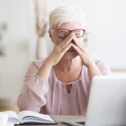 Tired senior woman rubbing her eyes as he works on her laptop.