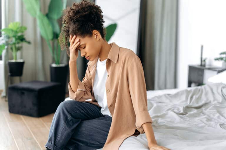 Woman with tinnitus sitting on the bed with her hand on her forehead