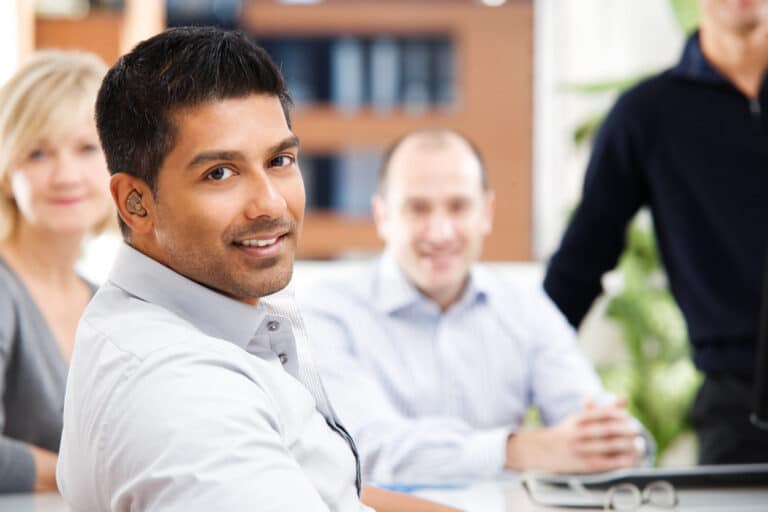 Smiling man wearing a hearing aid sitting with friends